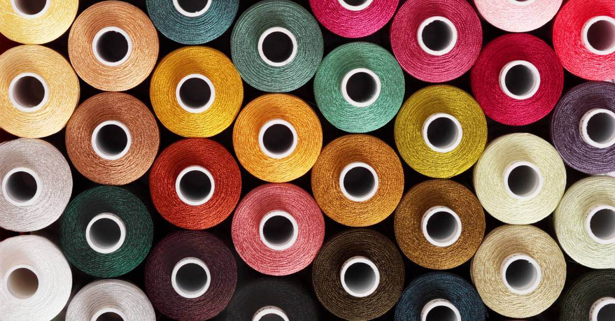 A top-down view of a collection of embroidery thread spools in various shades of soft-, earth-, and jewel-tone colors.