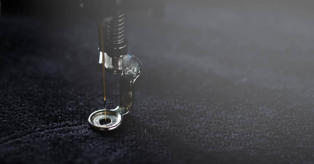 An embroidery machine needle is stitching a fine, yellow thread into a black piece of fabric.