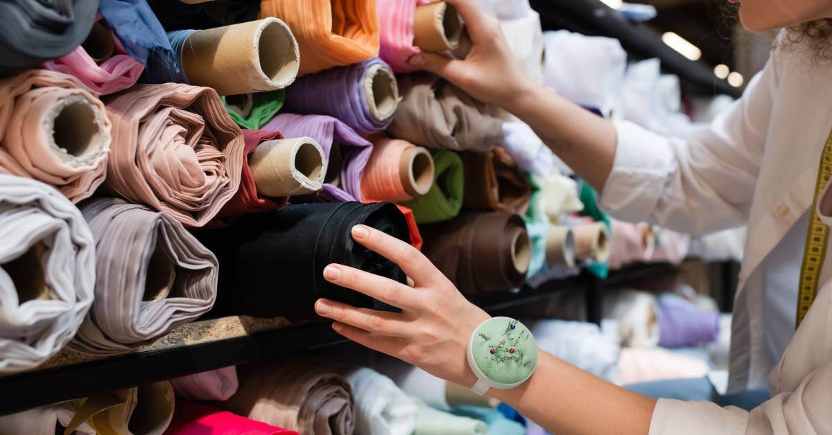 A woman in a textile shop is searching through various shelves full of colorful rolls of fabric.